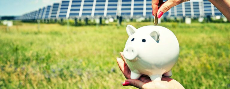 Vor einen großen Solarpark wird ein Sparschwein gehalten in das eine Münze geworfen wird, die durch Förderungsmaßnahmen der Anlage eingespart wurde.